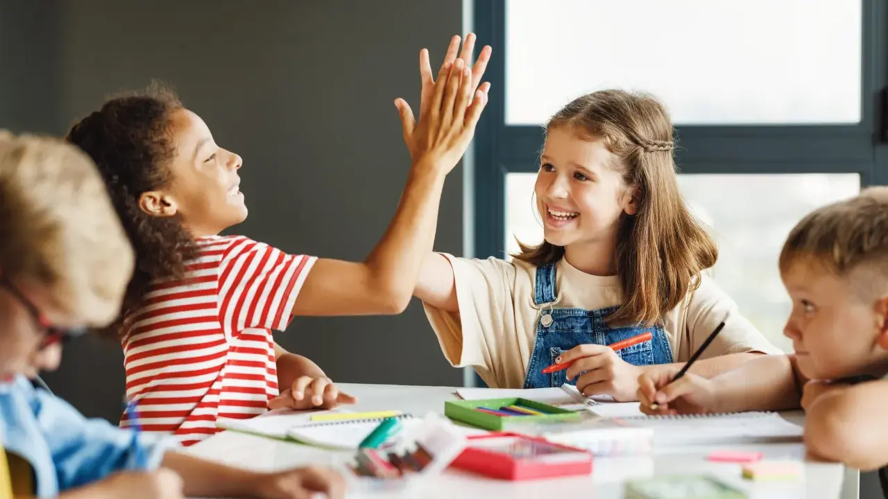 Zwei Grundschülerinnen geben sich einen High-Five, während sie konzentriert lernen. Ein tolles Beispiel für förderunterricht Grundschule, bei dem Spaß und Erfolg Hand in Hand gehen.