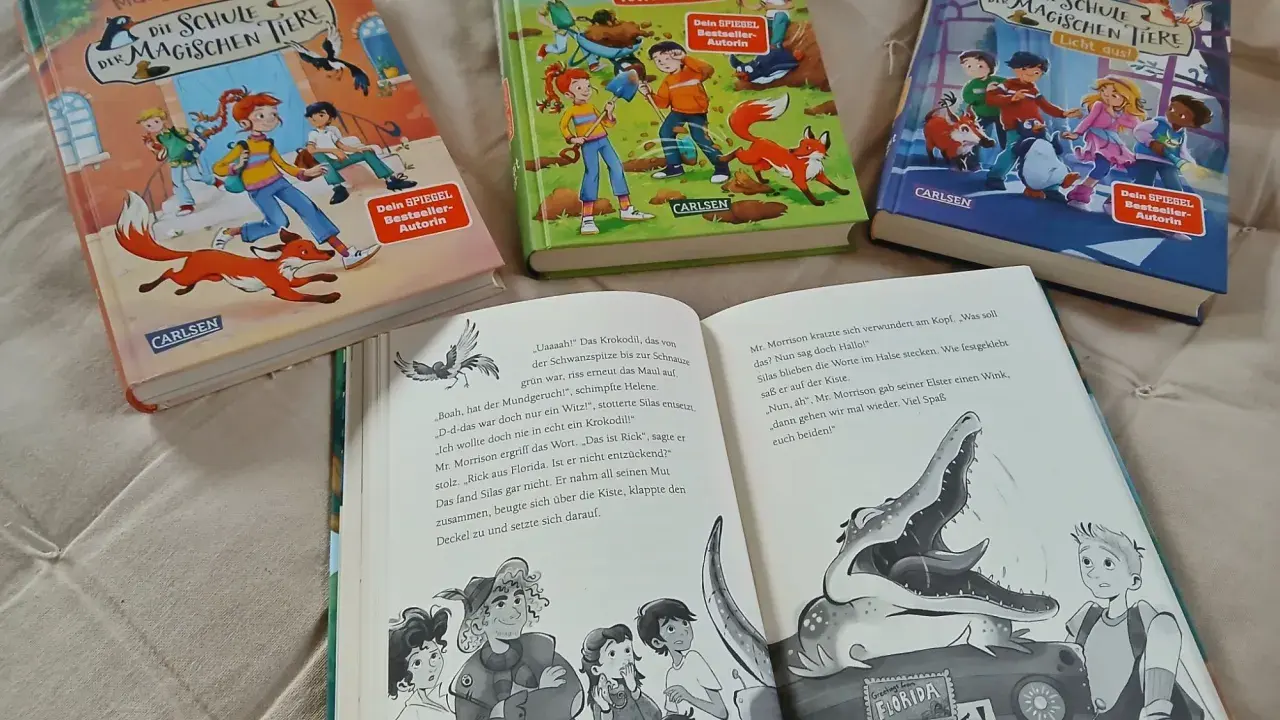 Drei Bücher der Reihe "Die Schule der magischen Tiere" von Margit Auer liegen nebeneinander. Aufgeschlagen ist ein Band mit einem Krokodil und einem Jungen.