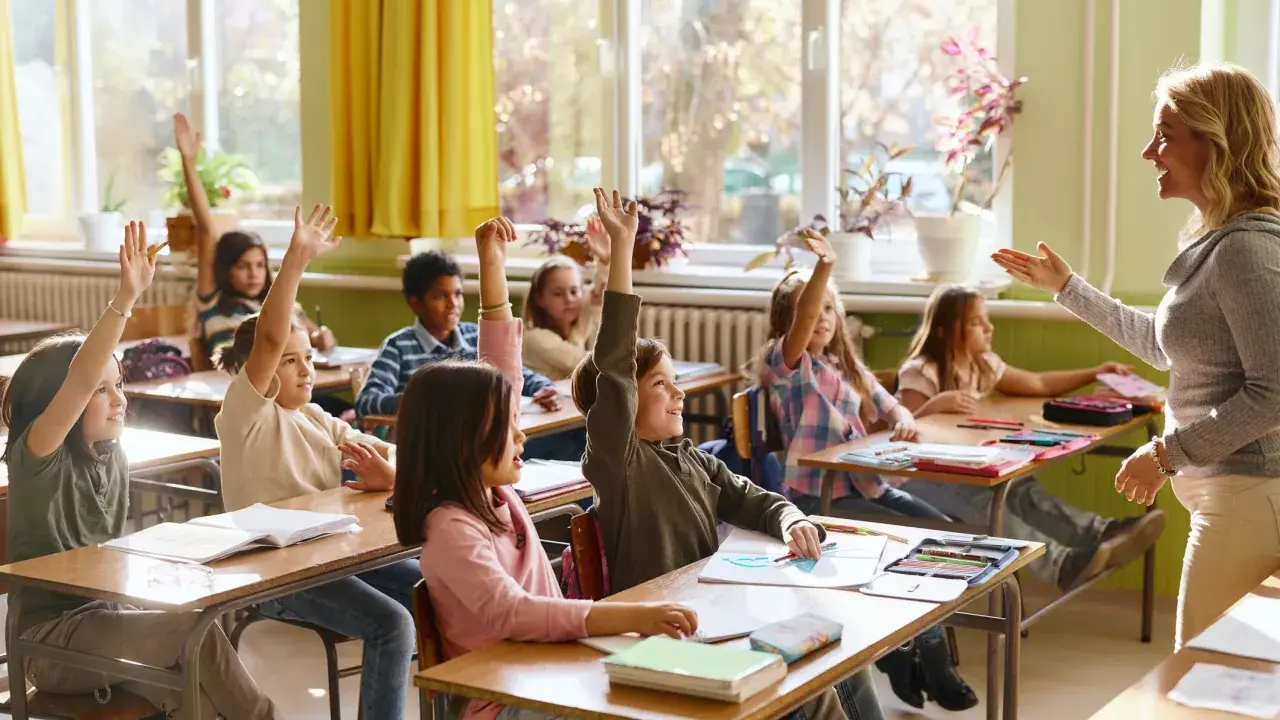 Grundschüler melden sich eifrig, ihre Sitzordnung zur Wand hin ausgerichtet, während die Lehrerin lächelt.