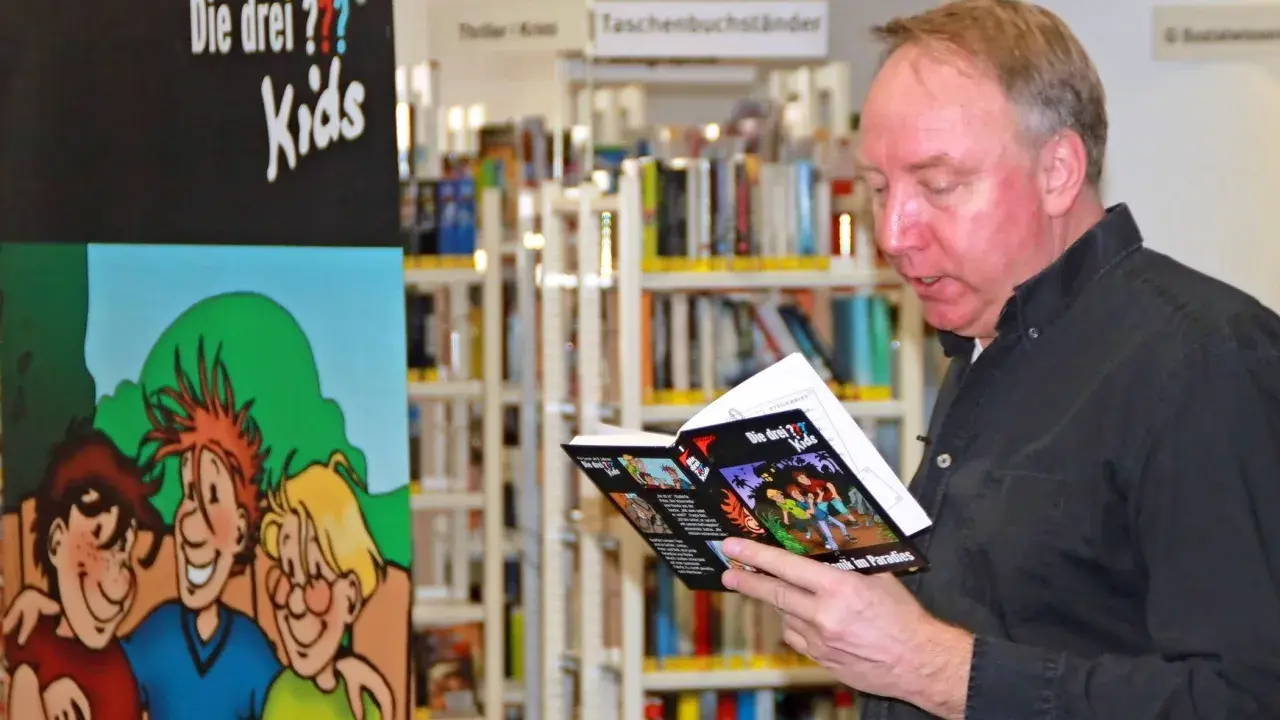 Ulf Blank liest ein Buch der "Die drei ??? Kids" in einer Bibliothek.