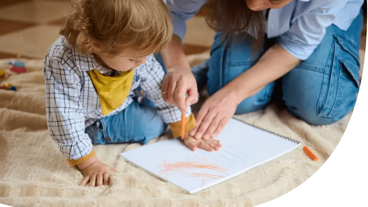 Ein Kind malt mit einem Wachsmalstift auf einem Blatt Papier, während eine Erwachsene ihm hilft. So können sie kinder motivieren mitzumachen.