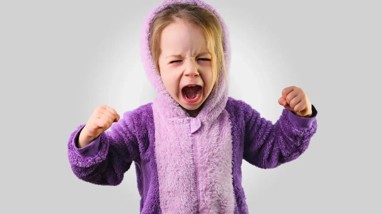 Kleines Kind im lila Pyjama schreit wütend, Fäuste geballt. Ein Ausdruck starker Emotionen bei Kindern.
