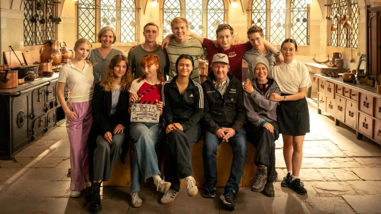 Das Team von "Die Schule der magischen Tiere" posiert in einer historischen Küche. Ein Mädchen hält eine Klappe mit dem Titel.