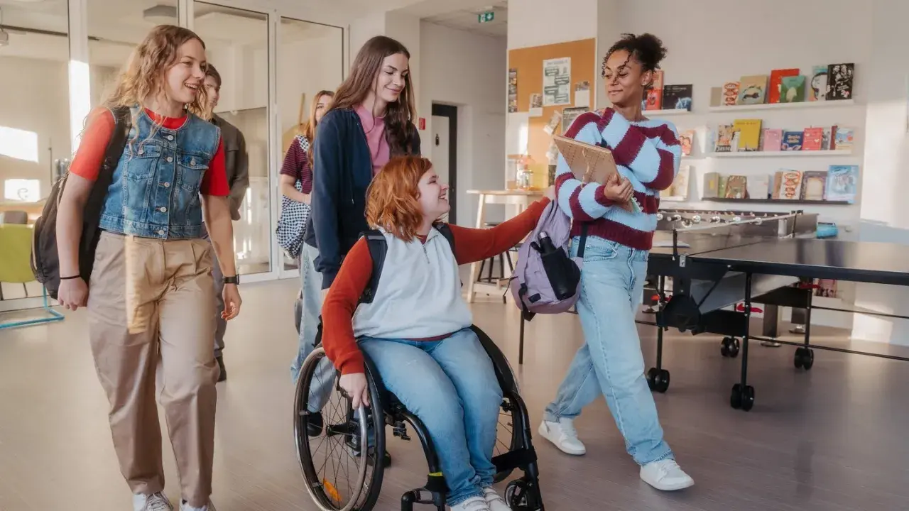 Schülerinnen gehen lachend durch den Flur. Eine im Rollstuhl, was **Inklusion an Schulen** zeigt.