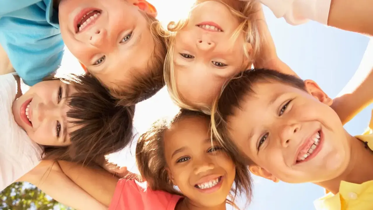 Fünf lachende Kinder blicken von oben in die Kamera. Sie zeigen, wie einfach es ist, Freunde in der Schule zu finden: mit einem Lächeln!