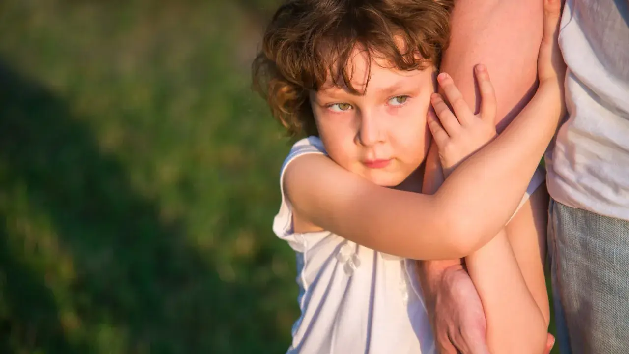 Ein Kind umklammert einen Arm, die Augen voller Kummer. Der **Trennungsschmerz bei Kindern** ist deutlich zu spüren.