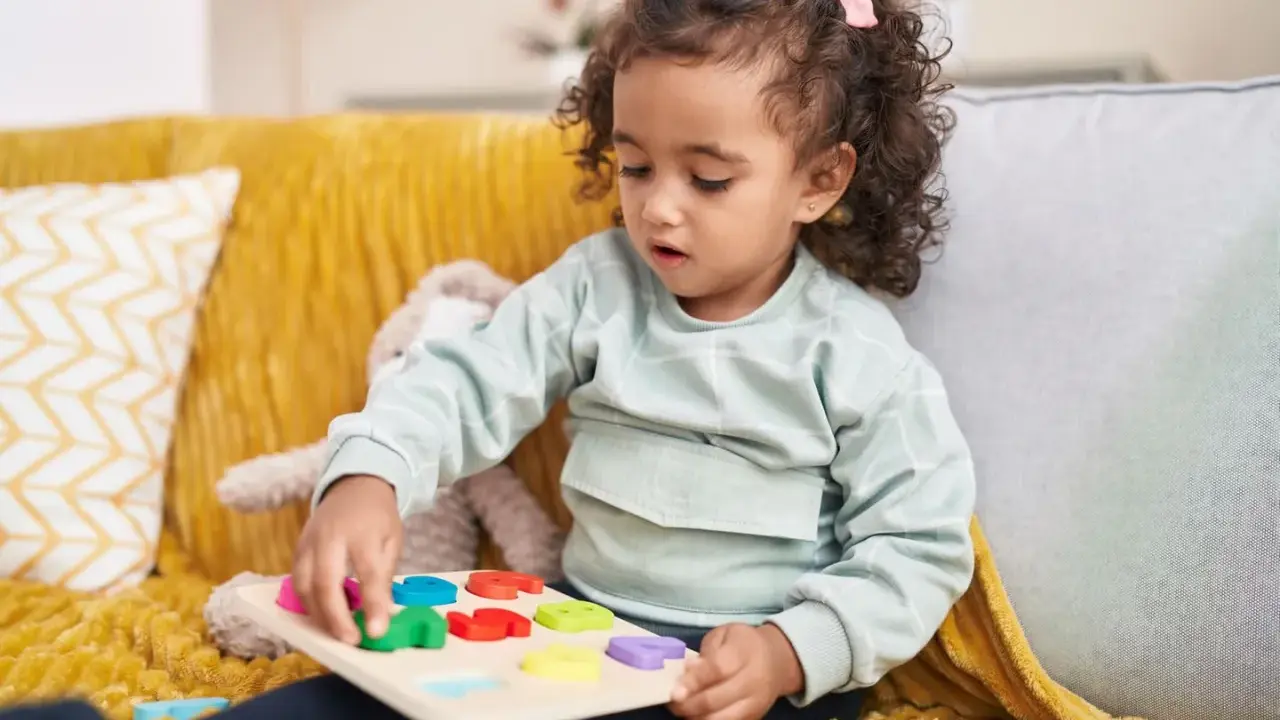 Kleines Mädchen mit Locken spielt konzentriert mit einem bunten Steckpuzzle. Das Spielzeug hilft, die **Konzentration zu steigern**.