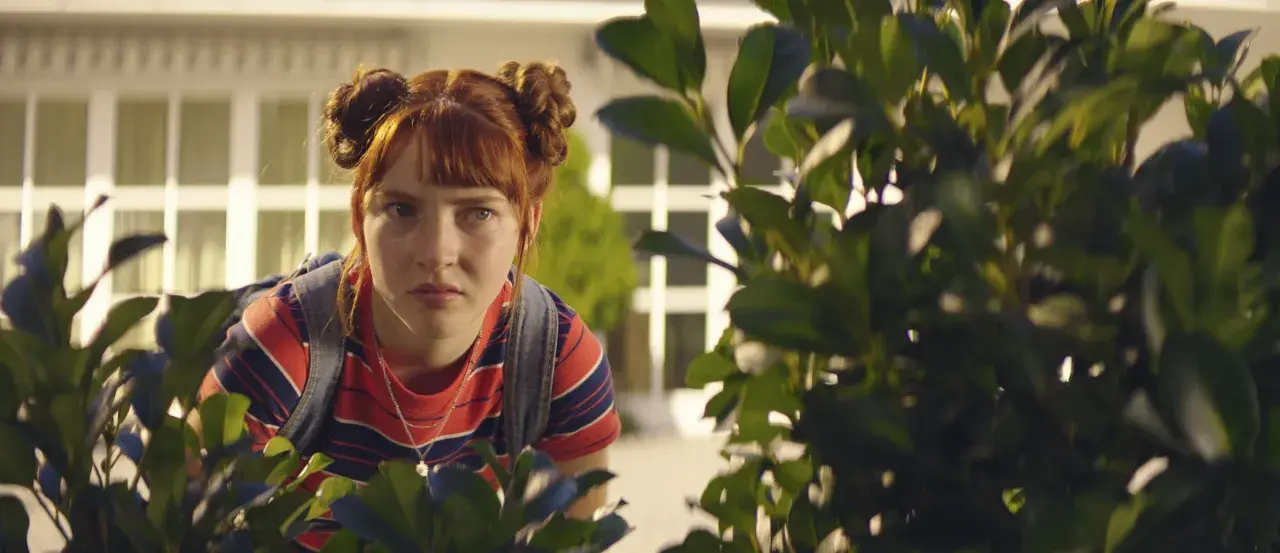 Ida aus "Die Schule der magischen Tiere" späht neugierig hinter Büschen hervor.