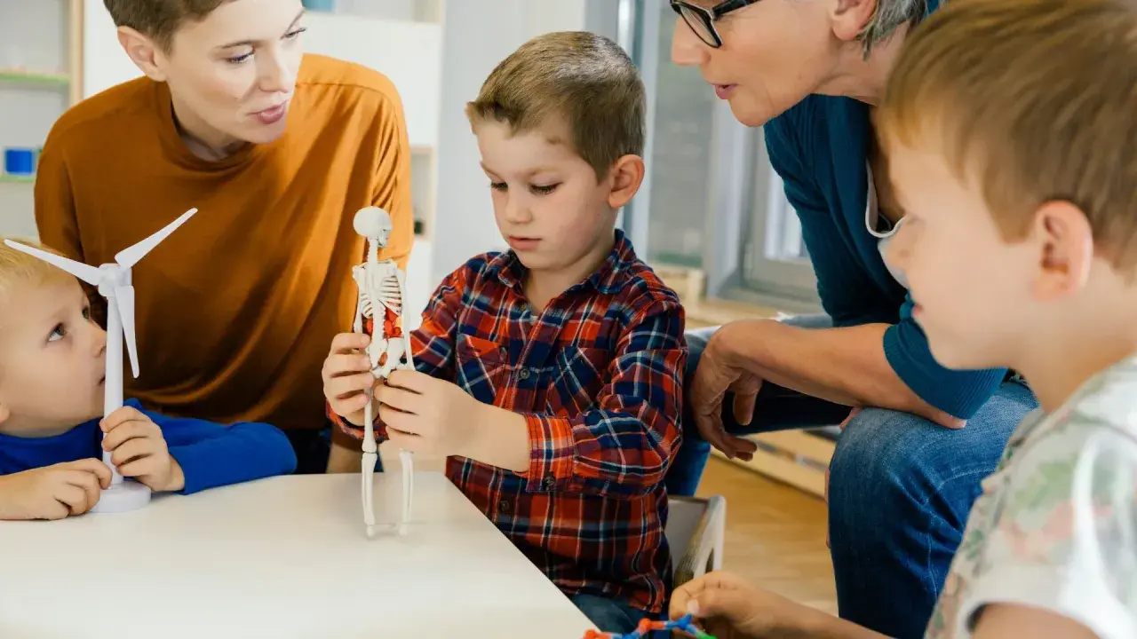 Kinder lernen mit einem Skelettmodell und einem Windrad. Die Lehrerin erklärt geduldig, wie wichtig es ist, sich auf Details zu konzentrieren, auch bei ads adhs.