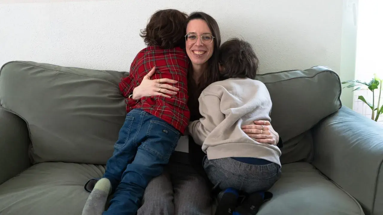 Eine Frau umarmt liebevoll zwei Kinder auf einer Couch. Ein Beispiel, wie man mit ADHS umgehen kann: durch Geborgenheit und Verständnis.