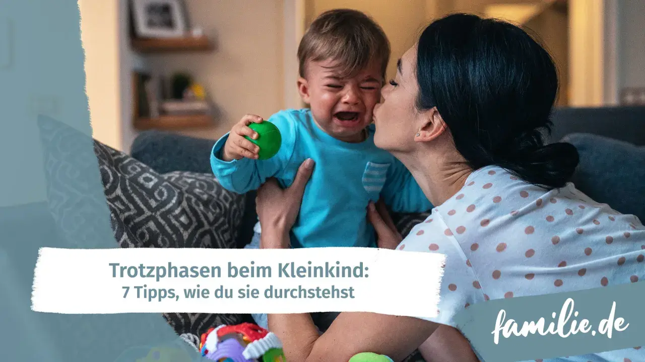 Mutter tröstet weinendes Kind, das einen grünen Ball hält. Ein Beispiel für den emotionalen quotient eines Kleinkindes.