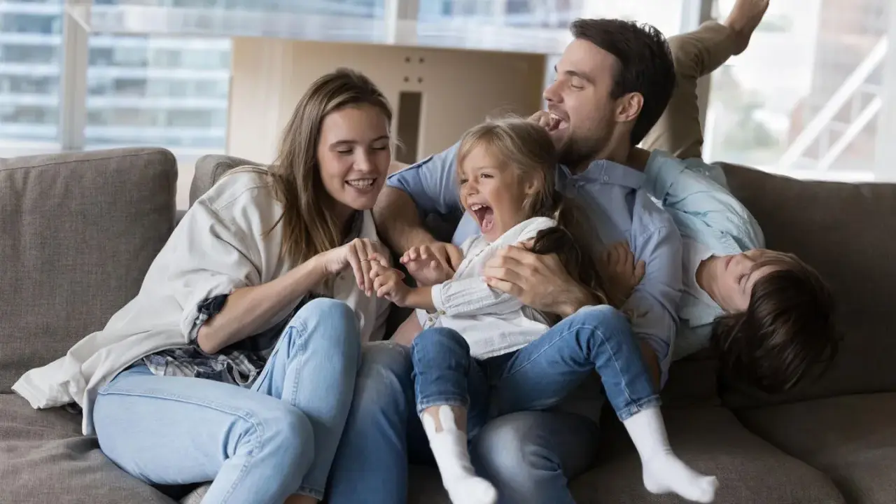 Eine Familie lacht und spielt auf dem Sofa. Das gemeinsame Lachen ist ein schönes Ritual.