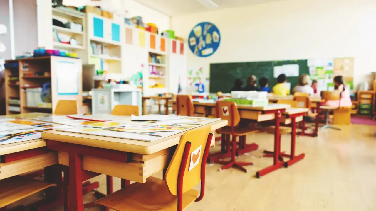 Leere Schultische und Stühle in einem Klassenzimmer, bereit für eine sitzordnung unruhige klasse. Kinder sitzen im Hintergrund.