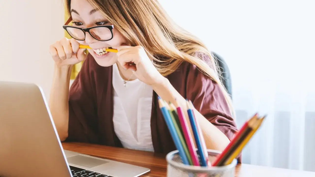 Junge Frau mit Brille bei der Arbeit, kaut auf einem Bleistift. Sie repräsentiert verschiedene lerntypen, die sich auf unterschiedliche Weise konzentrieren.