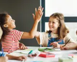 Zwei Grundschülerinnen geben sich einen High-Five, während sie konzentriert lernen. Ein tolles Beispiel für förderunterricht Grundschule, bei dem Spaß und Erfolg Hand in Hand gehen.