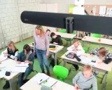 Lehrerin betreut Schüler im Klassenzimmer, die an ihren Tischen arbeiten. Ein modernes Setup für **hybrid unterricht**.