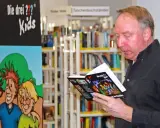 Ulf Blank liest ein Buch der "Die drei ??? Kids" in einer Bibliothek.