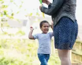 Ein wütendes Kind schreit und hebt die Arme, während eine Person Seifenblasen macht. Warum haut mein Kind mich 2 Jahre?