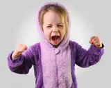 Kleines Kind im lila Pyjama schreit wütend, Fäuste geballt. Ein Ausdruck starker Emotionen bei Kindern.