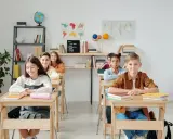 Schüler sitzen an Holztischen. Eine Lehrerin könnte hier kreative Sitzordnung Grundschule Ideen umsetzen.