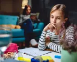 Ein nachdenkliches Kind sitzt am Schreibtisch, die Hand am Kinn. Es scheint, als ob das Kind sich selbst unter Druck setzt, während es lernt.
