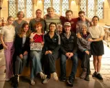 Das Team von "Die Schule der magischen Tiere" posiert in einer historischen Küche. Ein Mädchen hält eine Klappe mit dem Titel.