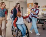 Schülerinnen gehen lachend durch den Flur. Eine im Rollstuhl, was **Inklusion an Schulen** zeigt.