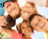 Fünf lachende Kinder blicken von oben in die Kamera. Sie zeigen, wie einfach es ist, Freunde in der Schule zu finden: mit einem Lächeln!