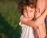 Ein Kind umklammert einen Arm, die Augen voller Kummer. Der **Trennungsschmerz bei Kindern** ist deutlich zu spüren.