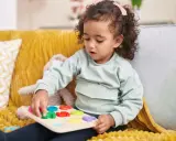 Kleines Mädchen mit Locken spielt konzentriert mit einem bunten Steckpuzzle. Das Spielzeug hilft, die **Konzentration zu steigern**.