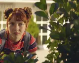 Ida aus "Die Schule der magischen Tiere" späht neugierig hinter Büschen hervor.