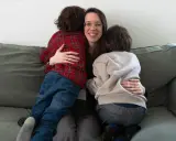Eine Frau umarmt liebevoll zwei Kinder auf einer Couch. Ein Beispiel, wie man mit ADHS umgehen kann: durch Geborgenheit und Verständnis.