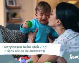 Mutter tröstet weinendes Kind, das einen grünen Ball hält. Ein Beispiel für den emotionalen quotient eines Kleinkindes.
