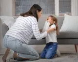 Frau tröstet weinendes Kind, das sich die Augen zuhält. Ein Gespräch über Probleme mit Eltern, was tun, kann helfen.