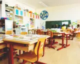 Leere Schultische und Stühle in einem Klassenzimmer, bereit für eine sitzordnung unruhige klasse. Kinder sitzen im Hintergrund.