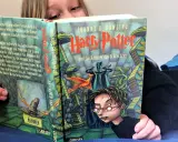 Ein Kind liest Harry Potter und die Kammer des Schreckens, eine Harry Potter Kinderversion. Der Zauberhut und ein Phönix sind auf dem Cover zu sehen.