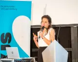 Eine Rednerin spricht über den Umgang mit Misserfolg. Im Hintergrund ein Banner der Deutschen Kinder- und Jugendstiftung.