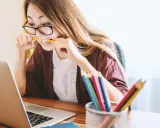 Junge Frau mit Brille bei der Arbeit, kaut auf einem Bleistift. Sie repräsentiert verschiedene lerntypen, die sich auf unterschiedliche Weise konzentrieren.