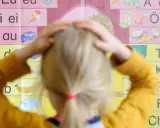 Ein Kind mit Händen am Kopf vor einer Buchstabenwand, die auf Schwierigkeiten beim Lesen und Schreiben (LRS) bei Kindern hindeuten könnte.