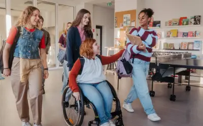 Schülerinnen gehen lachend durch den Flur. Eine im Rollstuhl, was **Inklusion an Schulen** zeigt.
