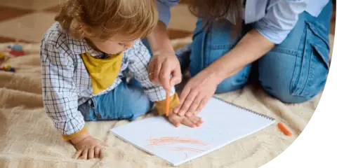 Ein Kind malt mit einem Wachsmalstift auf einem Blatt Papier, während eine Erwachsene ihm hilft. So können sie kinder motivieren mitzumachen.