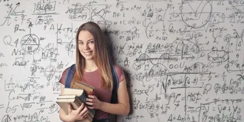 Ein lächelndes Mädchen mit Büchern vor einer Wand voller mathematischer Formeln. Sie zeigt, wie kann man sich in Mathe verbessern: durch Lernen und Üben.