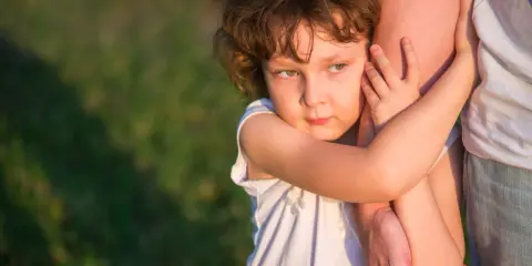 Ein Kind umklammert einen Arm, die Augen voller Kummer. Der **Trennungsschmerz bei Kindern** ist deutlich zu spüren.