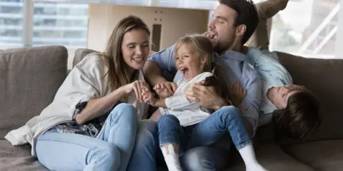 Eine Familie lacht und spielt auf dem Sofa. Das gemeinsame Lachen ist ein schönes Ritual.