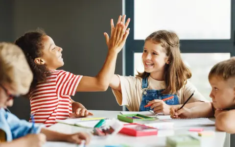 Zwei Grundschülerinnen geben sich einen High-Five, während sie konzentriert lernen. Ein tolles Beispiel für förderunterricht Grundschule, bei dem Spaß und Erfolg Hand in Hand gehen.