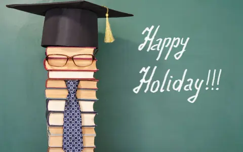 Ein Stapel Bücher mit Hut und Krawatte, der an die letzte Schulwoche erinnert. "Happy Holiday!!!" steht auf der Tafel.