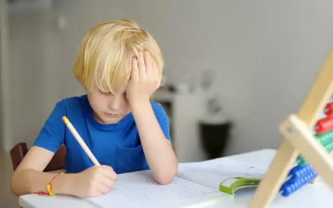 Junge mit blonden Haaren kämpft mit den Hausaufgaben. Mögliche ADHS-Ursachen und Erziehung sind hier ein Thema.