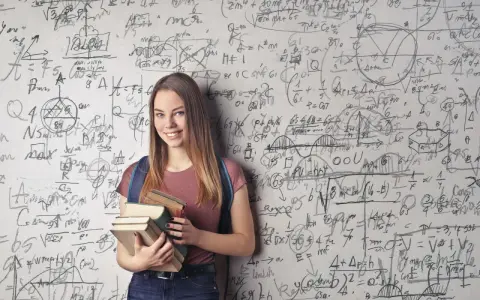 Ein lächelndes Mädchen mit Büchern vor einer Wand voller mathematischer Formeln. Sie zeigt, wie kann man sich in Mathe verbessern: durch Lernen und Üben.
