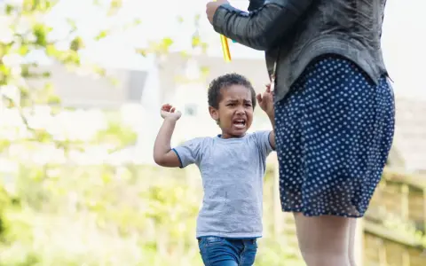Ein wütendes Kind schreit und hebt die Arme, während eine Person Seifenblasen macht. Warum haut mein Kind mich 2 Jahre?