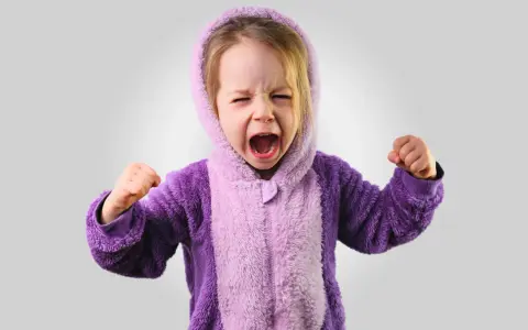 Kleines Kind im lila Pyjama schreit wütend, Fäuste geballt. Ein Ausdruck starker Emotionen bei Kindern.